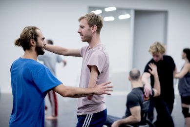 2 male dancers face each other holding hands.
