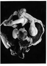 Several disabled and non- disabled dancers are intwined in a group. All wear plain black clothing.
