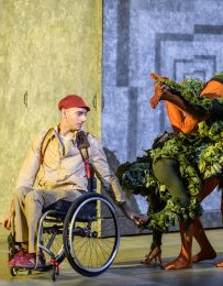Boy in wheelchair reaches out to green, plant-like creature