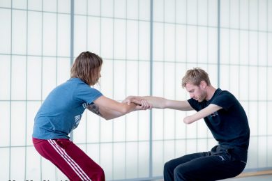Two dancers facing each other with bent knees as they pull against one another