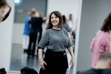Arlene Phillips, woman with brown shoulder length hair wearing silver long sleeved top stands with smile as she gazes to the side, holding arms to her side
