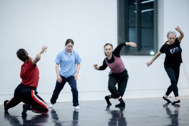 Four dancers in a light studio, all moving forward through space