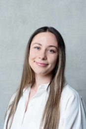 Louisa Sutherland has long, straight, light brown hair. She is smiling and wearing a white shirt
