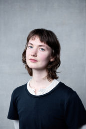 Susanna Dye. Susanna has pale blue eyes and dark hair. They are wearing a black tshirt with a white collar.