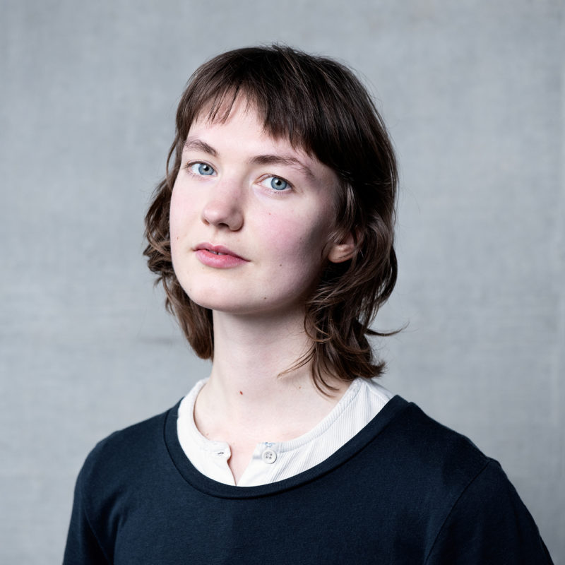 Susanna Dye. Susanna has pale blue eyes and dark hair. They are wearing a black tshirt with a white collar.