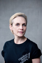 Caroline Lofthouse. A headshot of a smiling person with short blonde slicked back hair